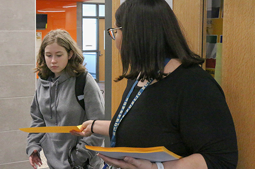 A teacher hands a student papers as she enters a classroom