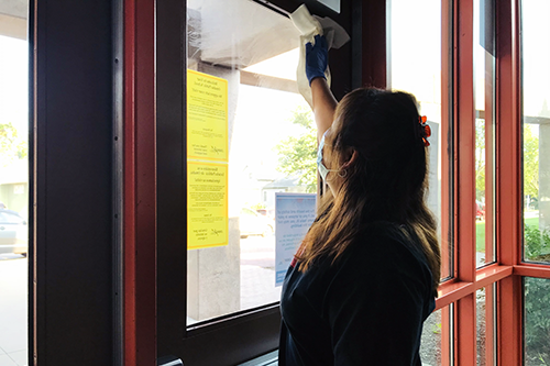 A staff member cleans the glass on a door to a school