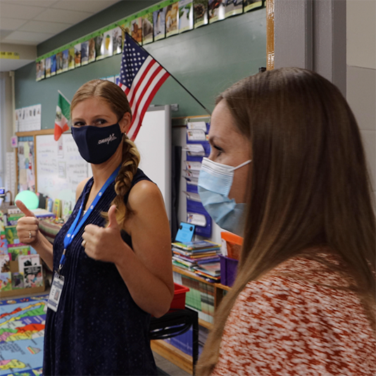  A principal gives a thumbs up as a teacher watches on.