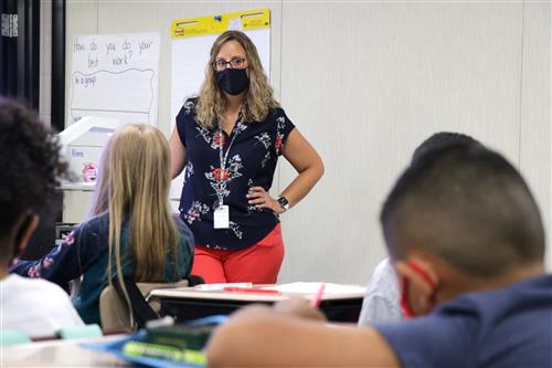 Teacher giving lesson to students in front of classroom.